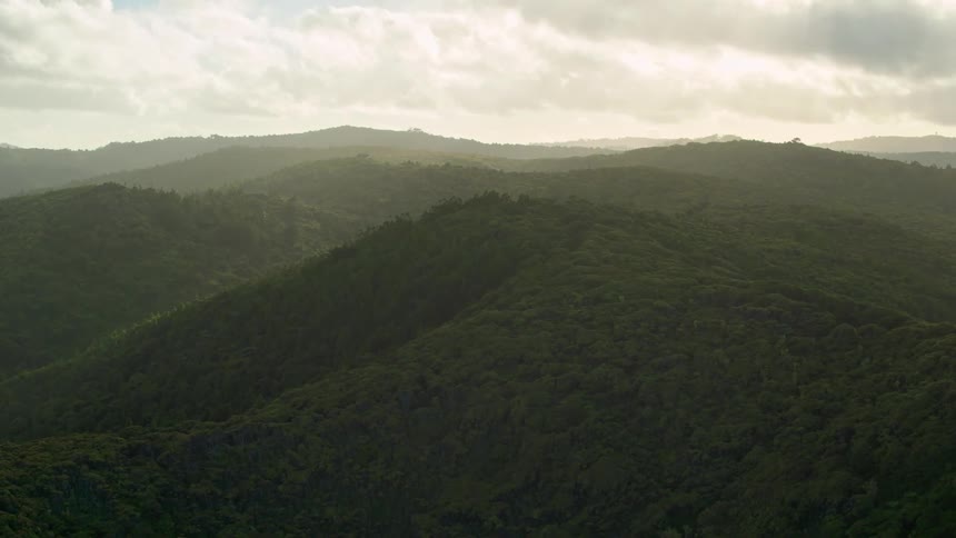 Clouds hover over hills covered with trees during the day
