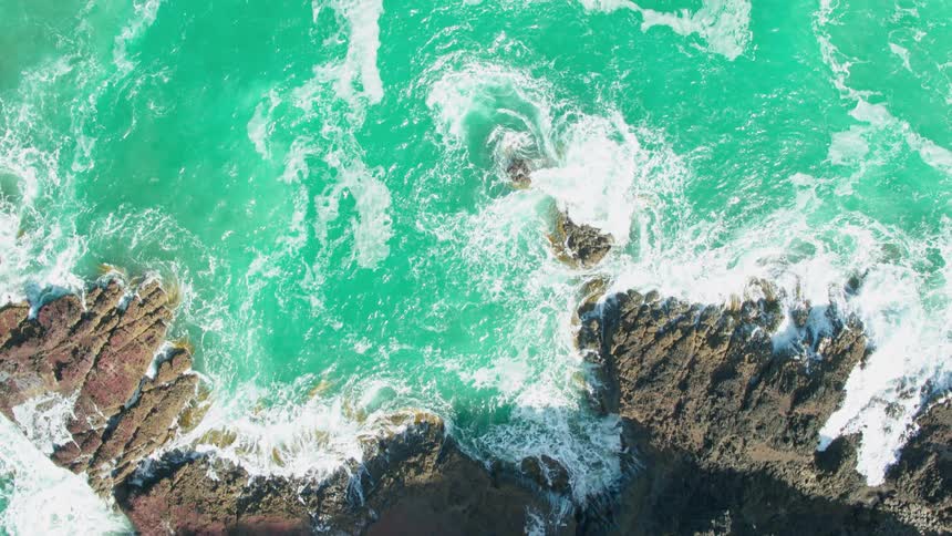 Ocean waves splash over rocks along the coast on a sunny day