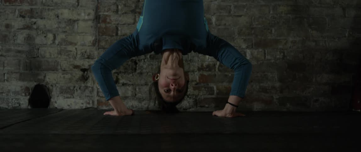 A woman does handstand pushups against a brick wall