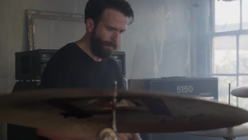 A man is playing drums in a room during the day