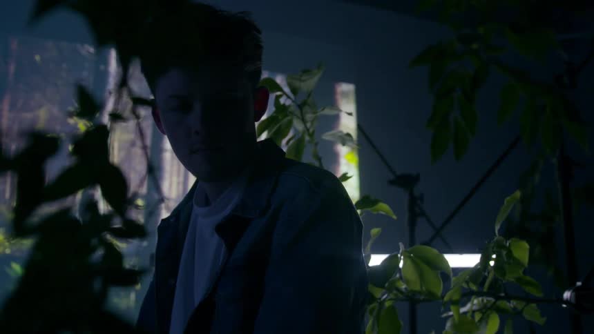 Young man sits while looking at leafy plants