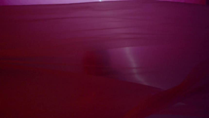 Fabric flows around a woman standing in front of a projection of lightning