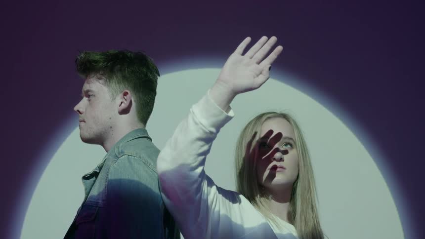 A young man and woman stand in front of a bright projection