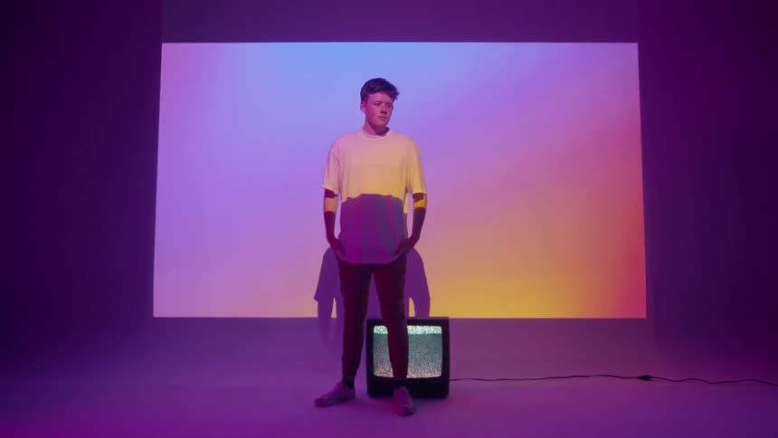 A young man stands in front of a television and a projection screen