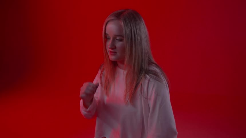 A young woman reaches up to move her hair as she sits in a red room