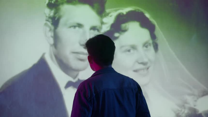 A young man stands in front of flashing projections on the wall