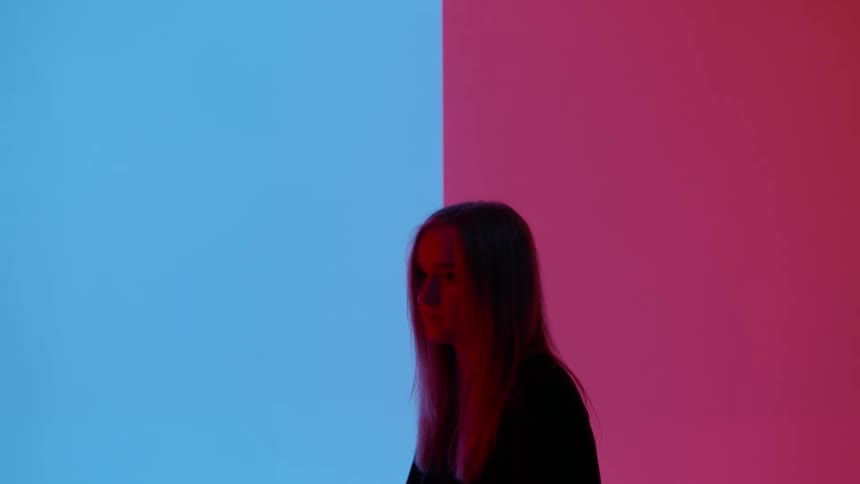 A young woman is sitting still in front of a colored wall