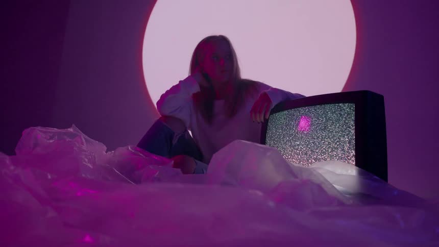 A woman sits in a purple room with a flickering tv
