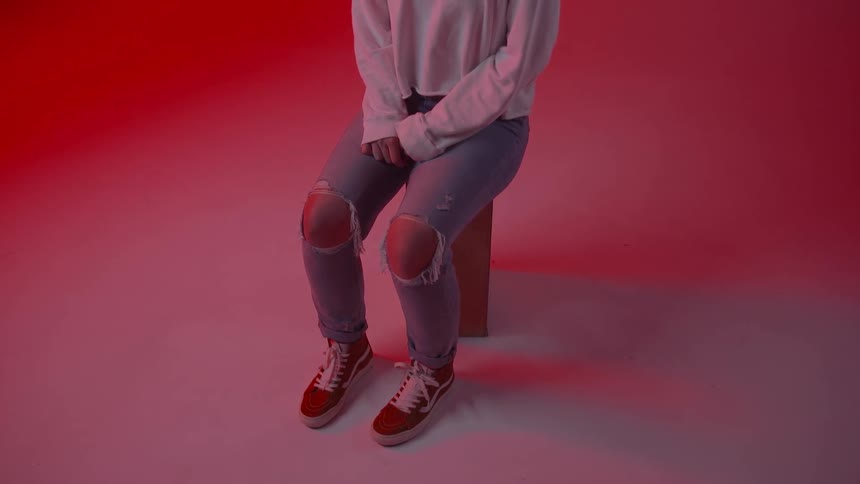 A young woman is sitting with her hands in her lap in a red room