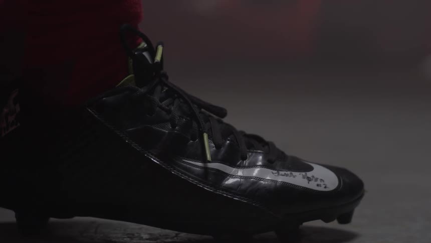A person wearing a cleated athletic shoe is standing still