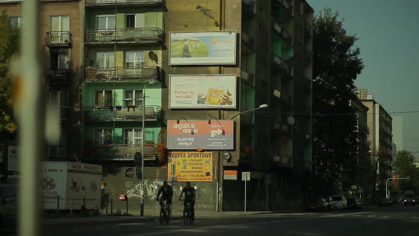 Two people bike down a city street in the daytime