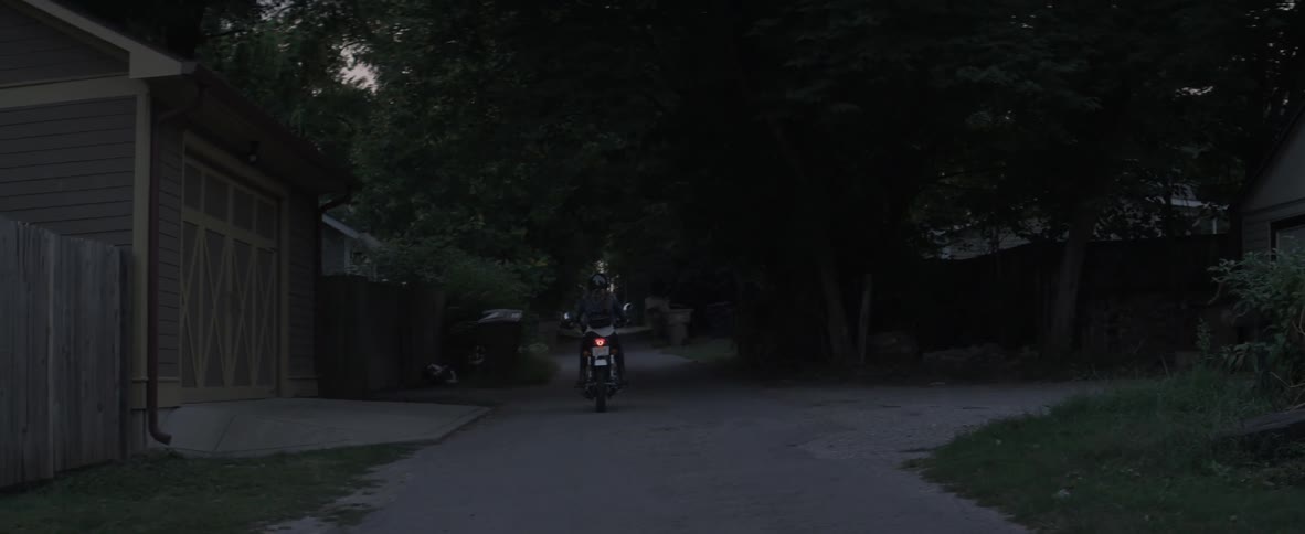A woman drives a motorcycle down a narrow suburban street