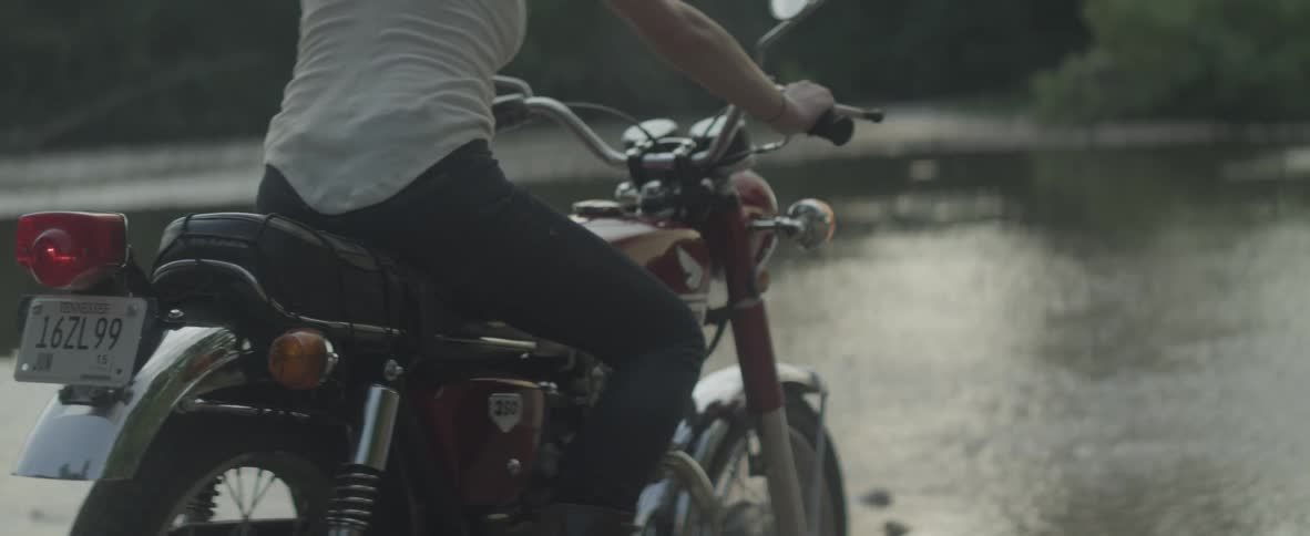 A woman rides off on a motorcycle into the water