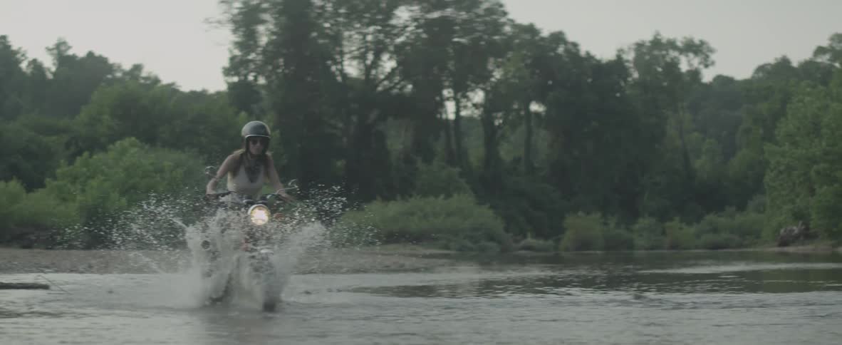 A woman rides a motorcycle into water