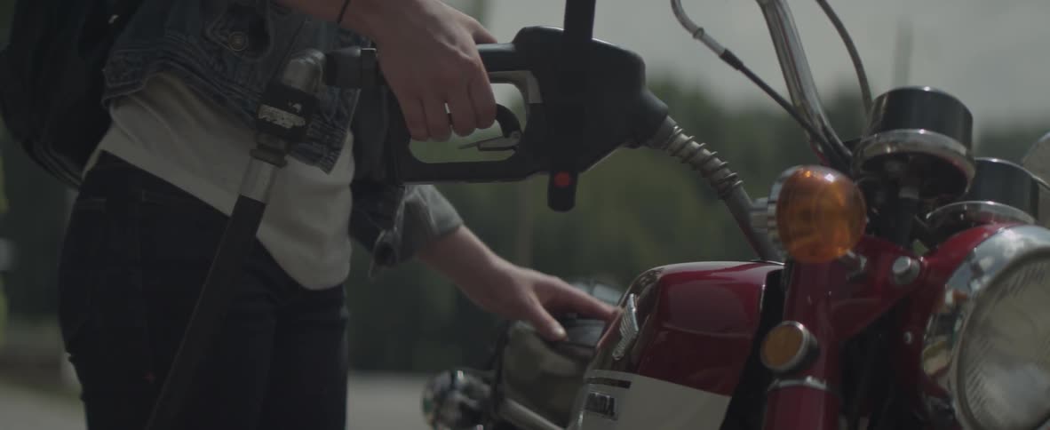A woman is filling her motorcycle's tank with fuel