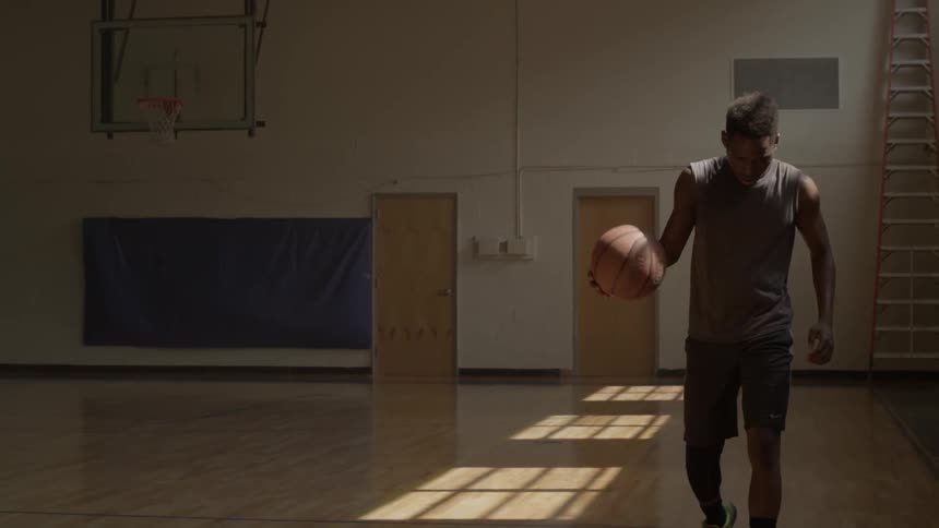A man is bouncing a basketball on a court indoors during the day
