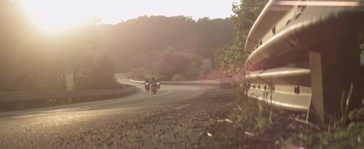 A group of motorcyclists travel on a rural road at dusk