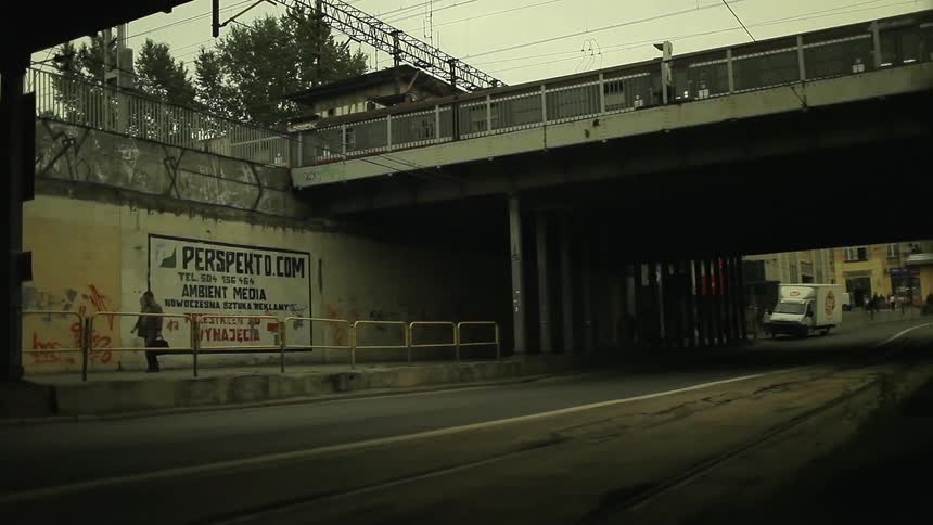 People walk in a city as a train passes overhead