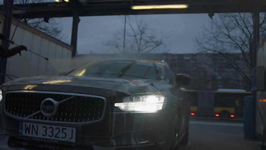 A man is washing a vehicle in a carwash at dusk