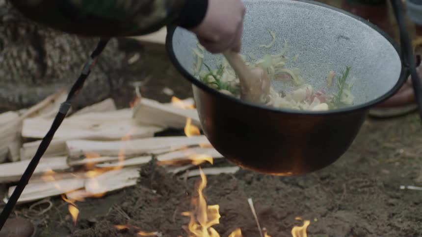 Man stirs food cooking over an open fire