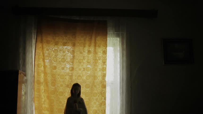 A religious statue sits in front of a curtained window