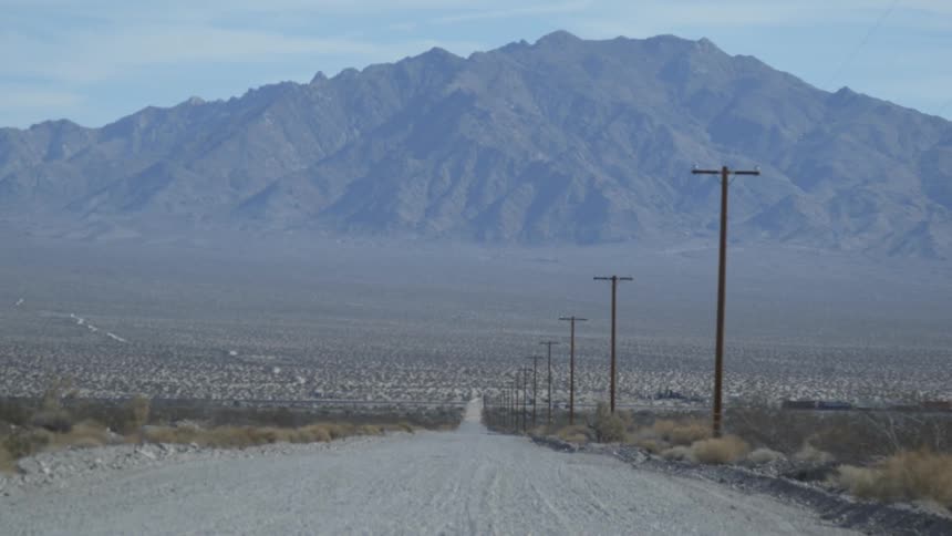 A train passes across a dirt road in the desert during the day