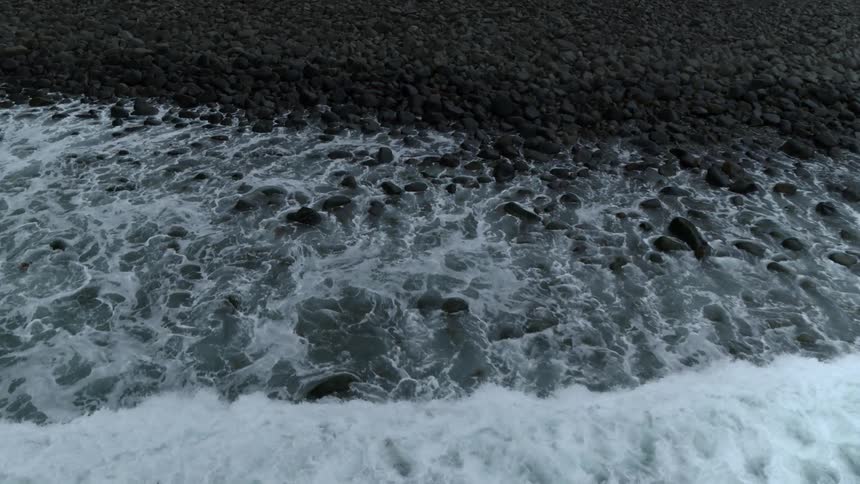 Waves crest and roll over rocks on a shore during the day