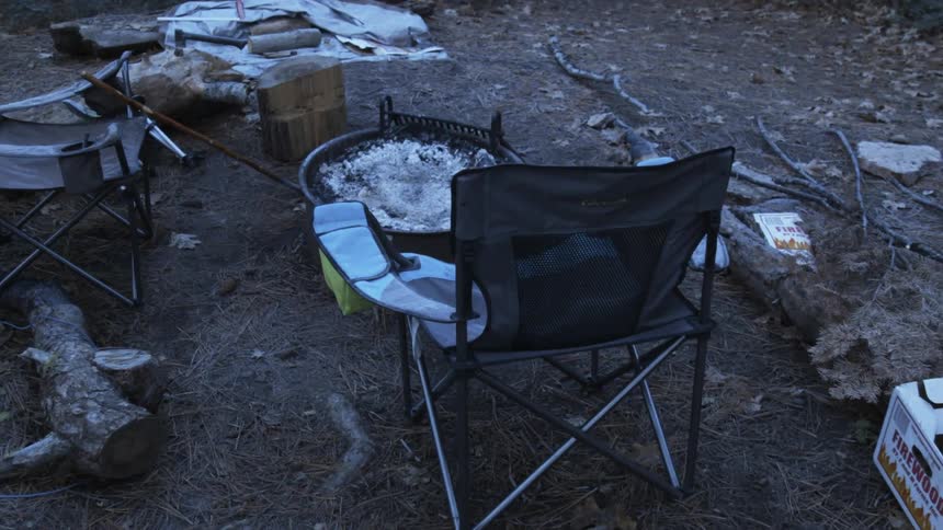Empty chairs sit close to a dormant campfire in a campground