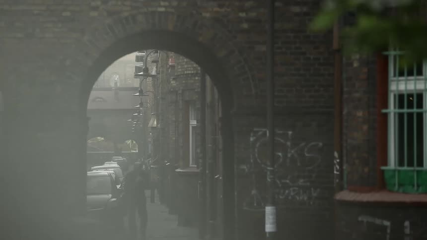 Smoking man walking towards archway on city street