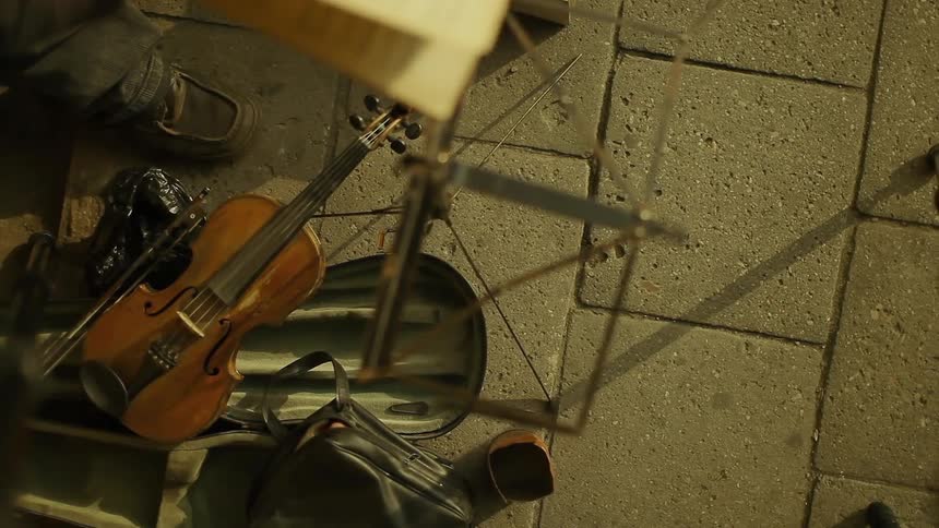 A violin lays on the ground next to a man's foot as he flips through sheet music