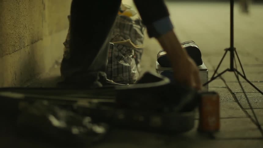 A subway musician reaches down to check his donation can