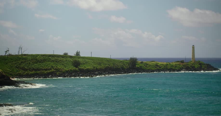 Waves lap a shoreline with a small tower during the day
