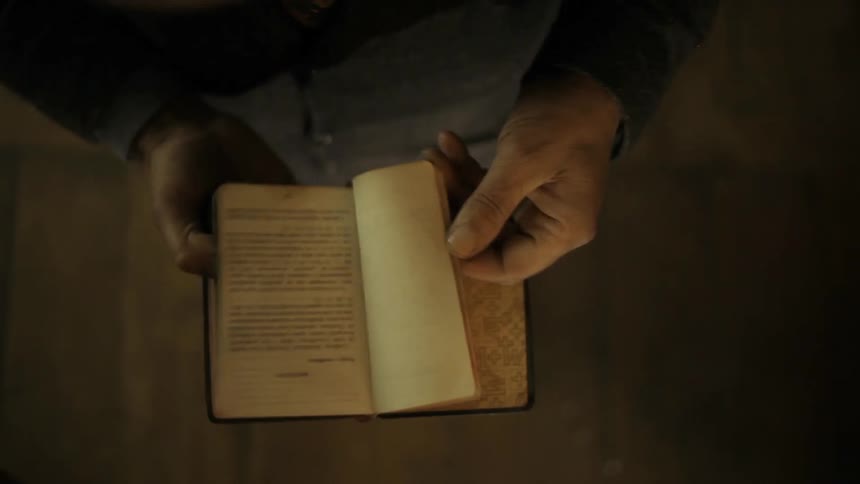 A man's hands flip through an old, worn book