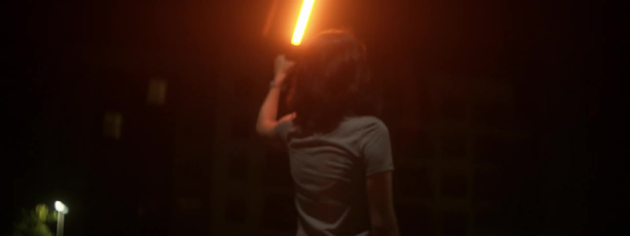 A woman holds a light beam aloft outside at night