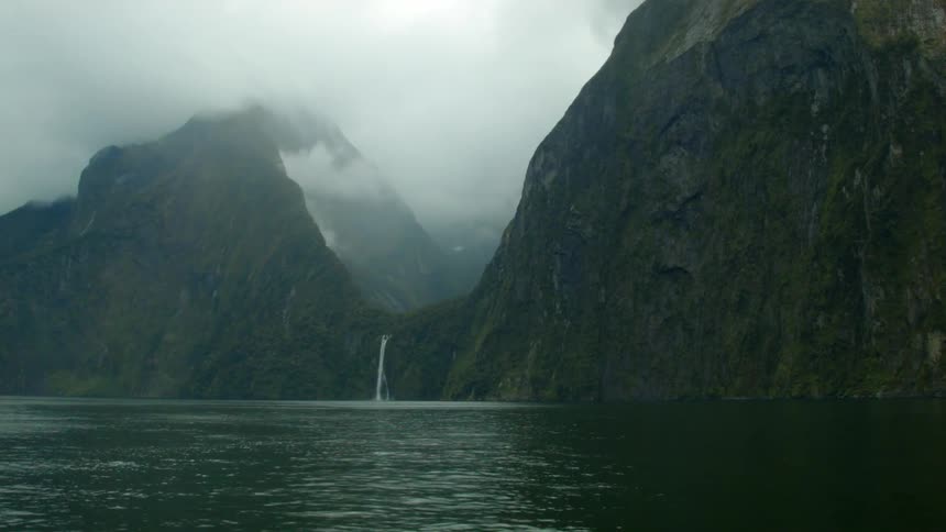 A waterfall cascade out of the mountains and into the ocean on a cloudy day