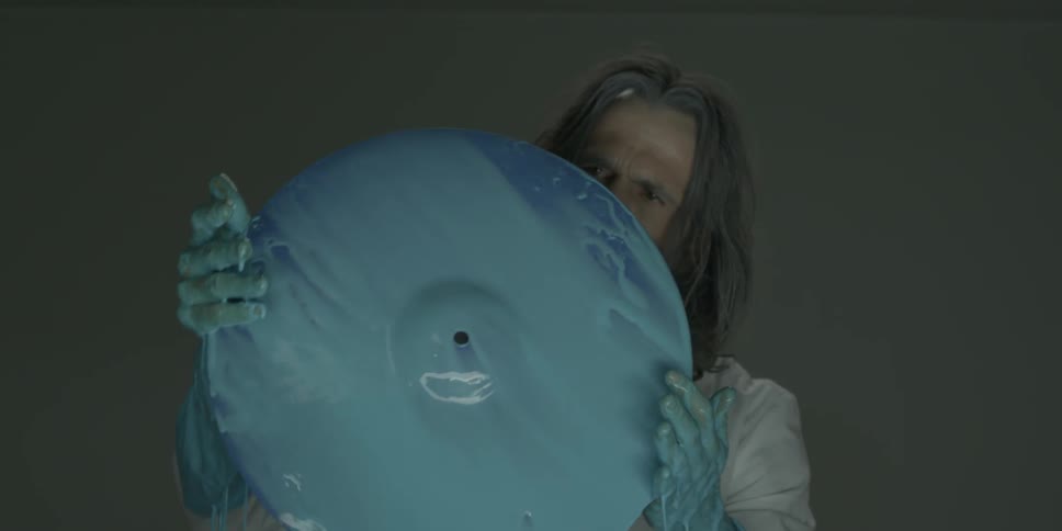 A man in a lab coat is examining a cymbal covered in blue liquid