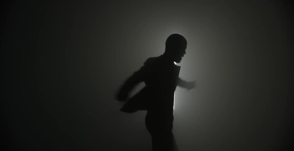 A man dances in a dark room with a large light