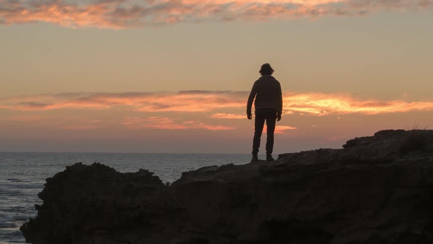 A man walks along a cliff by the ocean