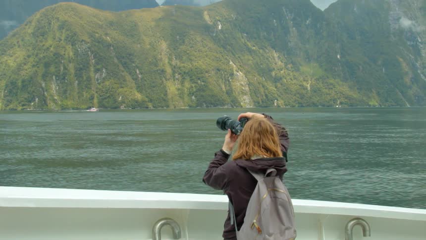 A woman is taking photos of a coastline from a boat