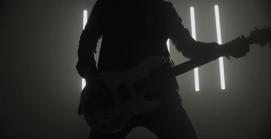 A person is playing a guitar in a dark room with a slatted window