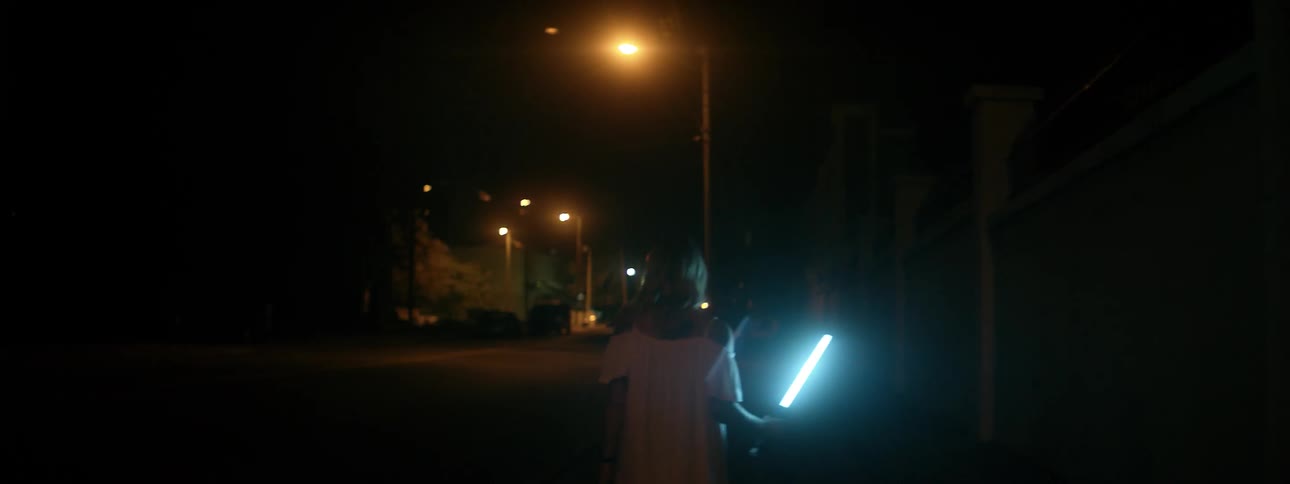 Woman walks on dark city street with a glowing light saber