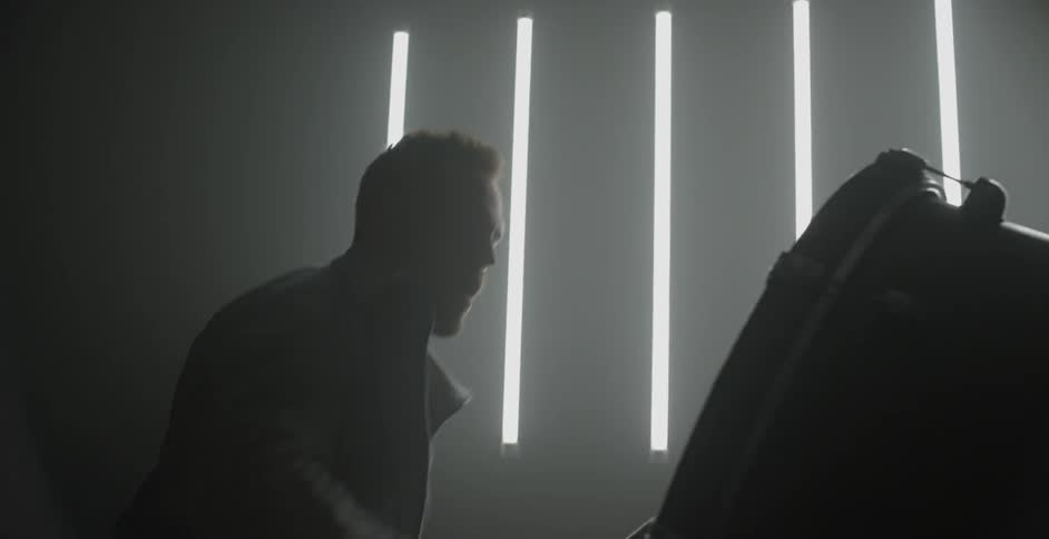 A man plays the drums in front of a wall with fluorescent light tubes