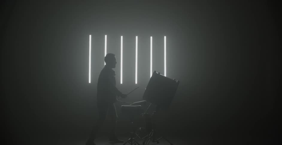 A man is standing up playing a drum set indoors