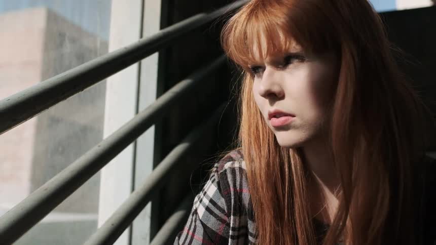 A woman sits in a stairwell window looking out at a city during the day