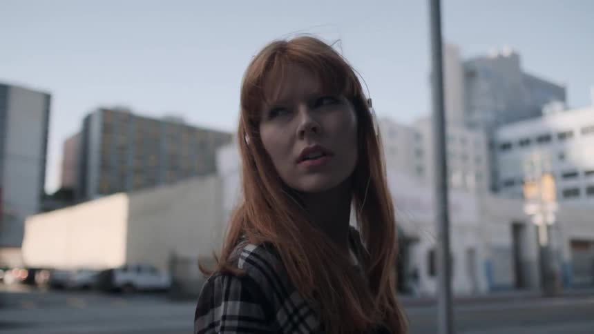 A red haired woman walks outside while wearing headphones