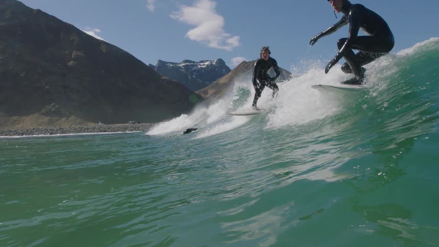 Surfers stand on their boards to catch a wave