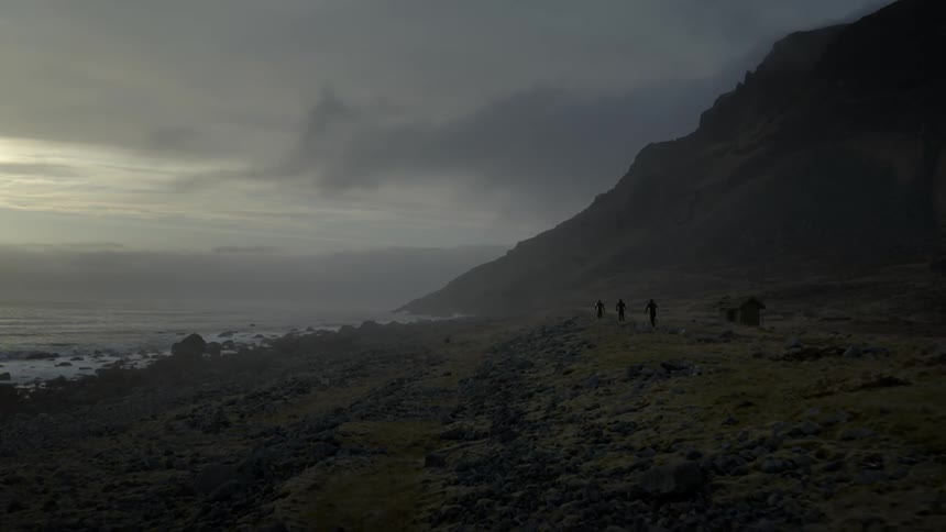 Men carrying surfboards hike along a rugged coastline