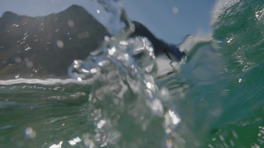 A surfer rides a wave in the sun then the crest of the wave crashes down on him