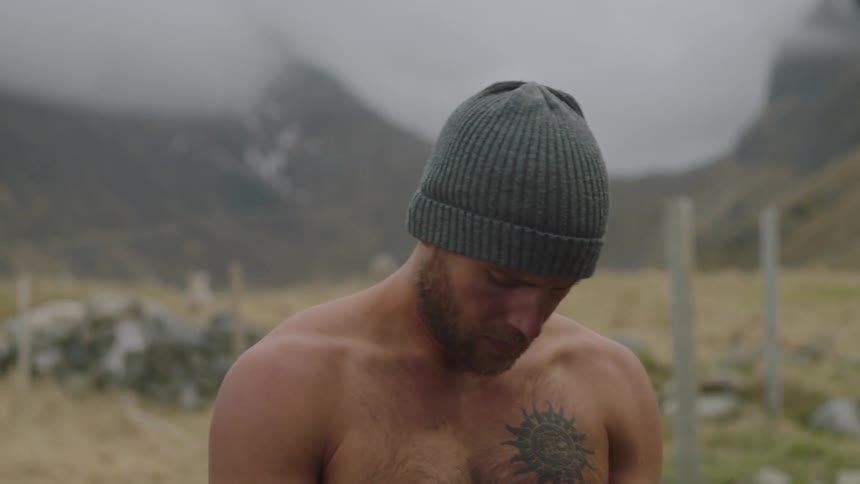 A man standing in a mountain valley is taking off his shirt
