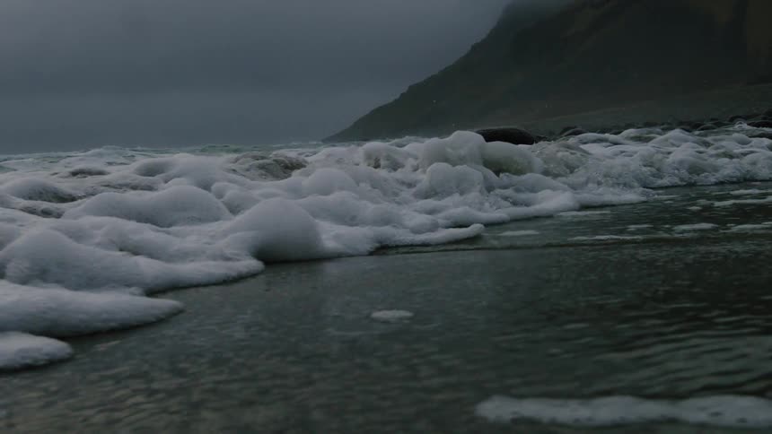 Waves carry foam onto a beach on a stormy day